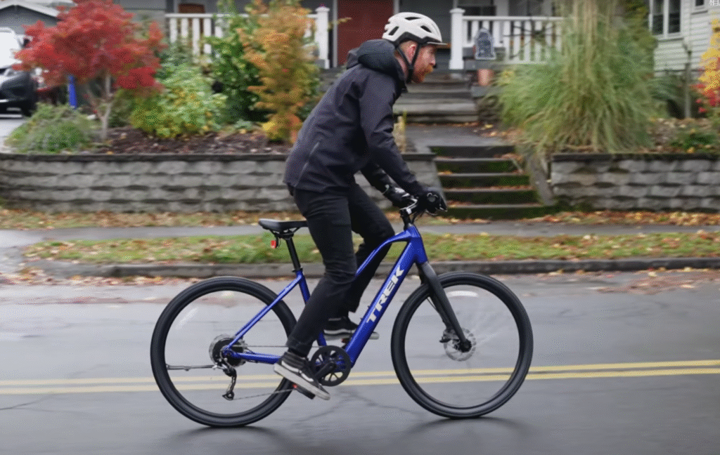 Cyclist riding a blue Trek FX+ electric commuter bike on a suburban street.