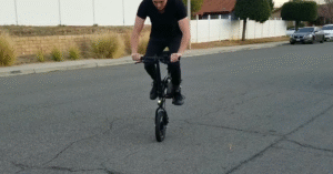 Man performing a wheelie on a compact folding electric bike on a suburban street, showcasing agility and fun riding style.