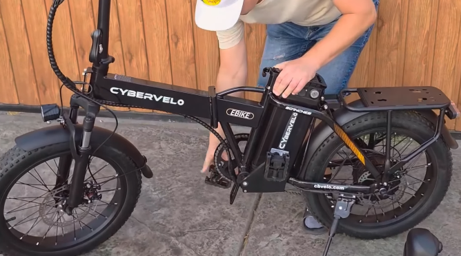 Man folding a Cybervelo 1000 Peak electric bike with fat tires and rear cargo rack.
