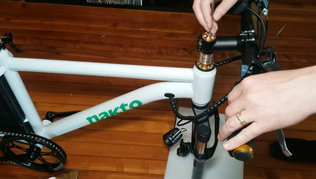 Nakto Electric Bike Reviews: Models, Value, Pros & Cons 2 Person assembling a Nakto electric bike by tightening the handlebar stem bolts during setup.