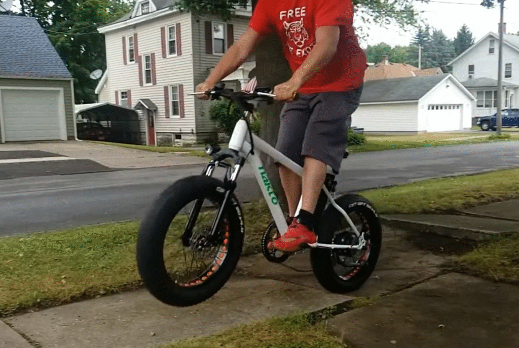 Rider testing a Nakto fat-tire electric bike by jumping off a curb on a neighborhood street.