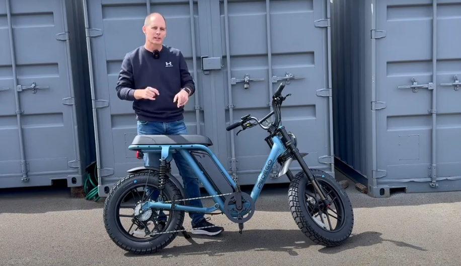 Pedego moped-style electric bike on kickstand while a tester explains features at a dealership lot.