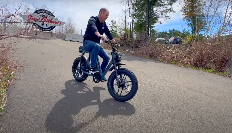 Rider test-rides a Pedego moped-style e-bike on a paved lot during a handling and throttle demo.