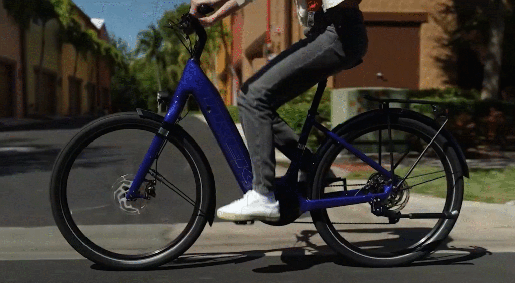 Trek Verve+ 3 electric bike in blue, being ridden on a city road with a stylish design and integrated rack.