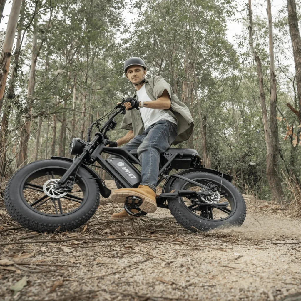 Man riding a fat-tire electric bike off-road through a forest trail, leaning into a turn.