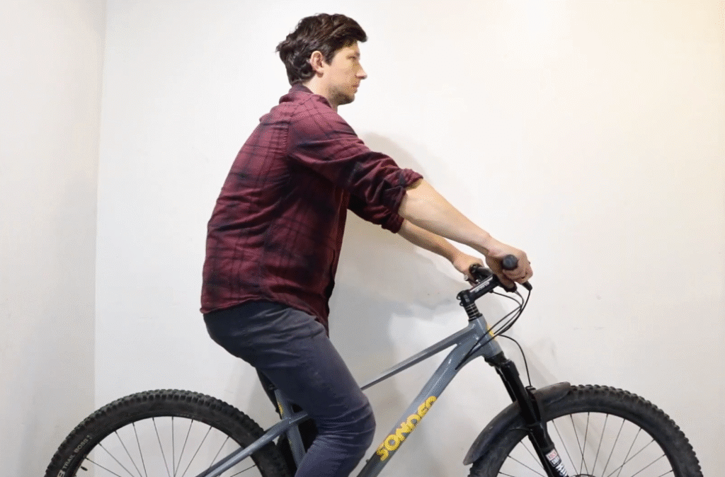 Cyclist in profile checking riding posture with hands on mountain bike handlebars.