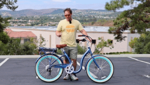 Man standing beside a blue beach cruiser electric bike in a parking lot