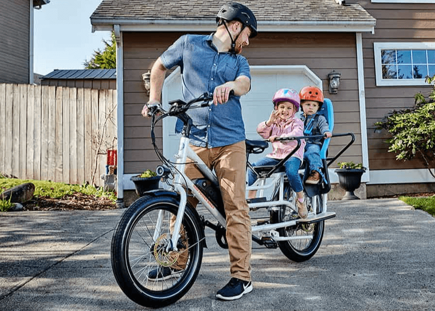 Father with two children on a compact family e-bike in front of a house.