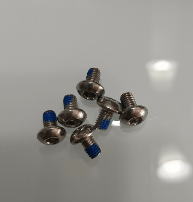 Set of small metal bolts with blue thread lock on a reflective surface.