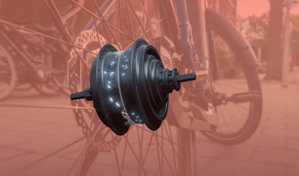 Pedal "Clunk" at Start on Belt-Drive E-Bikes: All Likely Causes & Fixes 3 Rendered image of an Enviolo Urban internal gear hub floating in front of a blurred bike background, showcasing its black cylindrical design with threaded axle and disc brake mounting points.